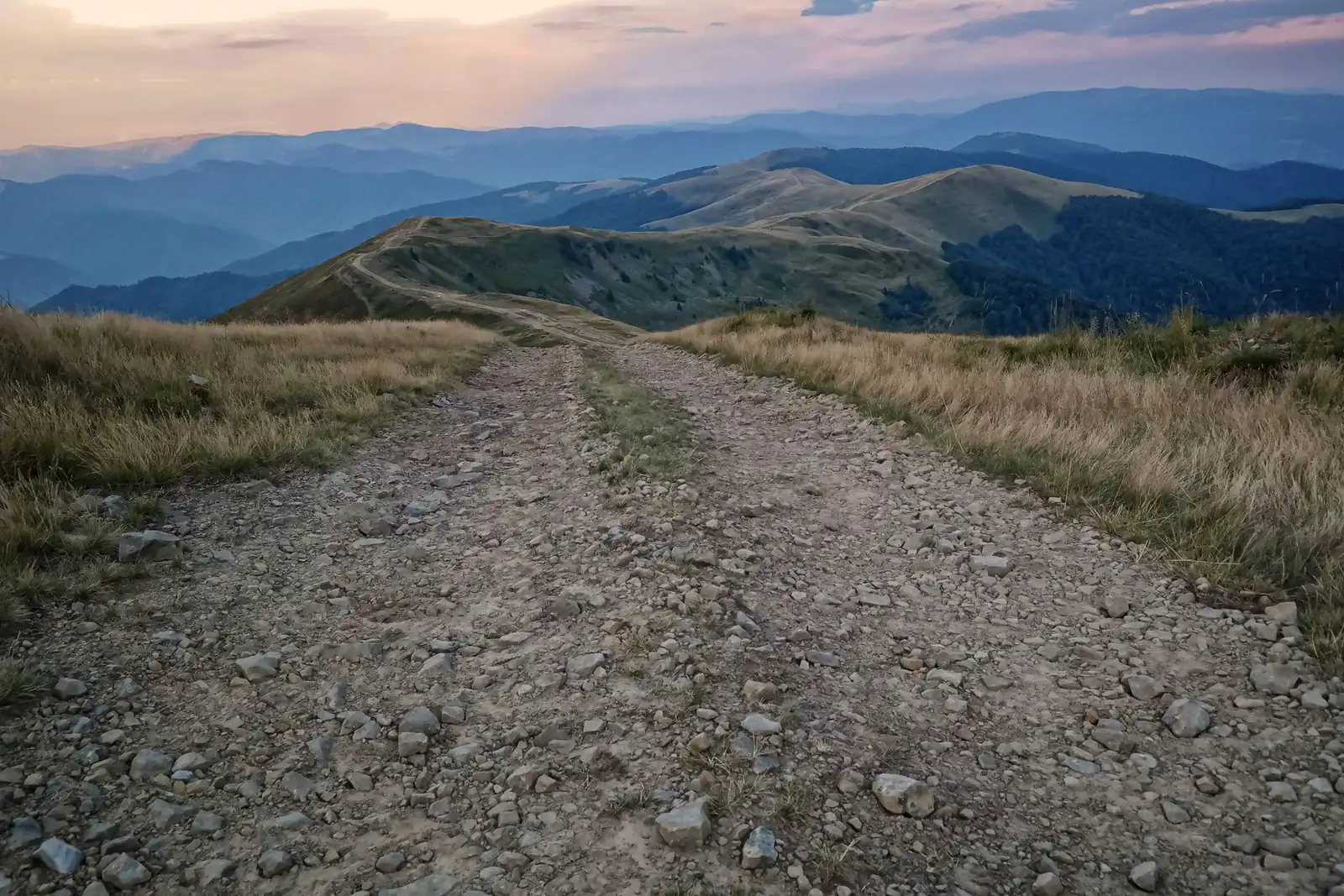 Gravel road running along a treeless mountain ridgeline into layered blue-hour haze