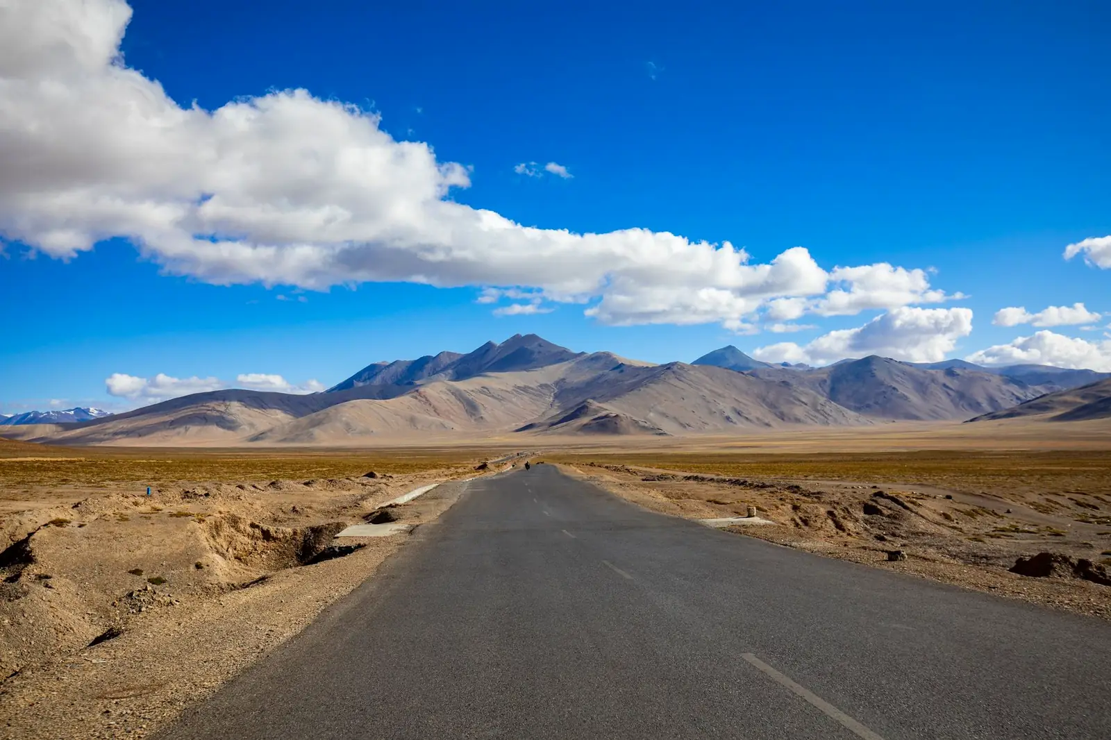 Paved two-lane highway stretching in a straight line across a high, treeless mountain plateau toward distant peaks