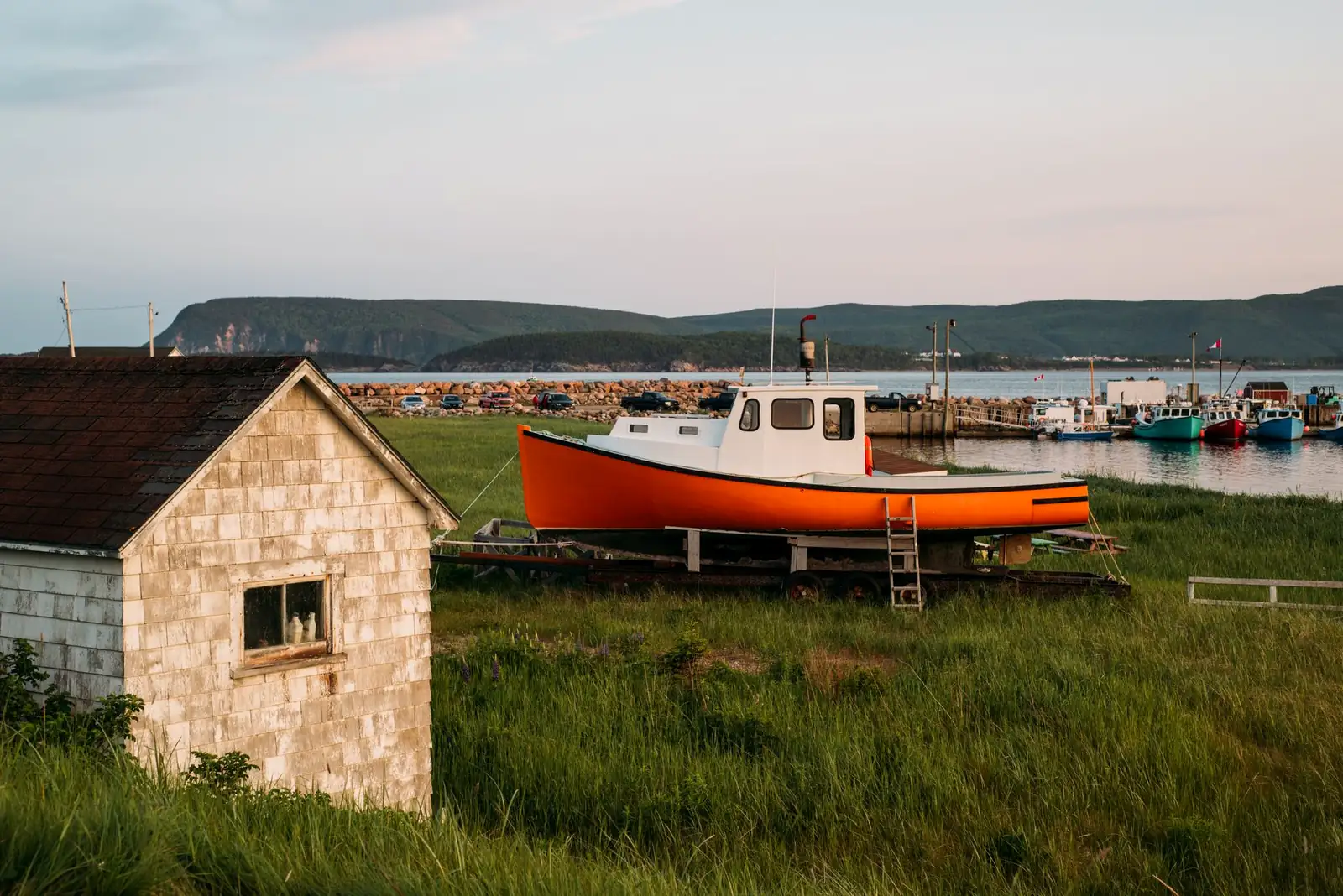 A fishing boat pulled up at a small Acadian harbor on Cape Breton's west coast at sunset, highlands in the background