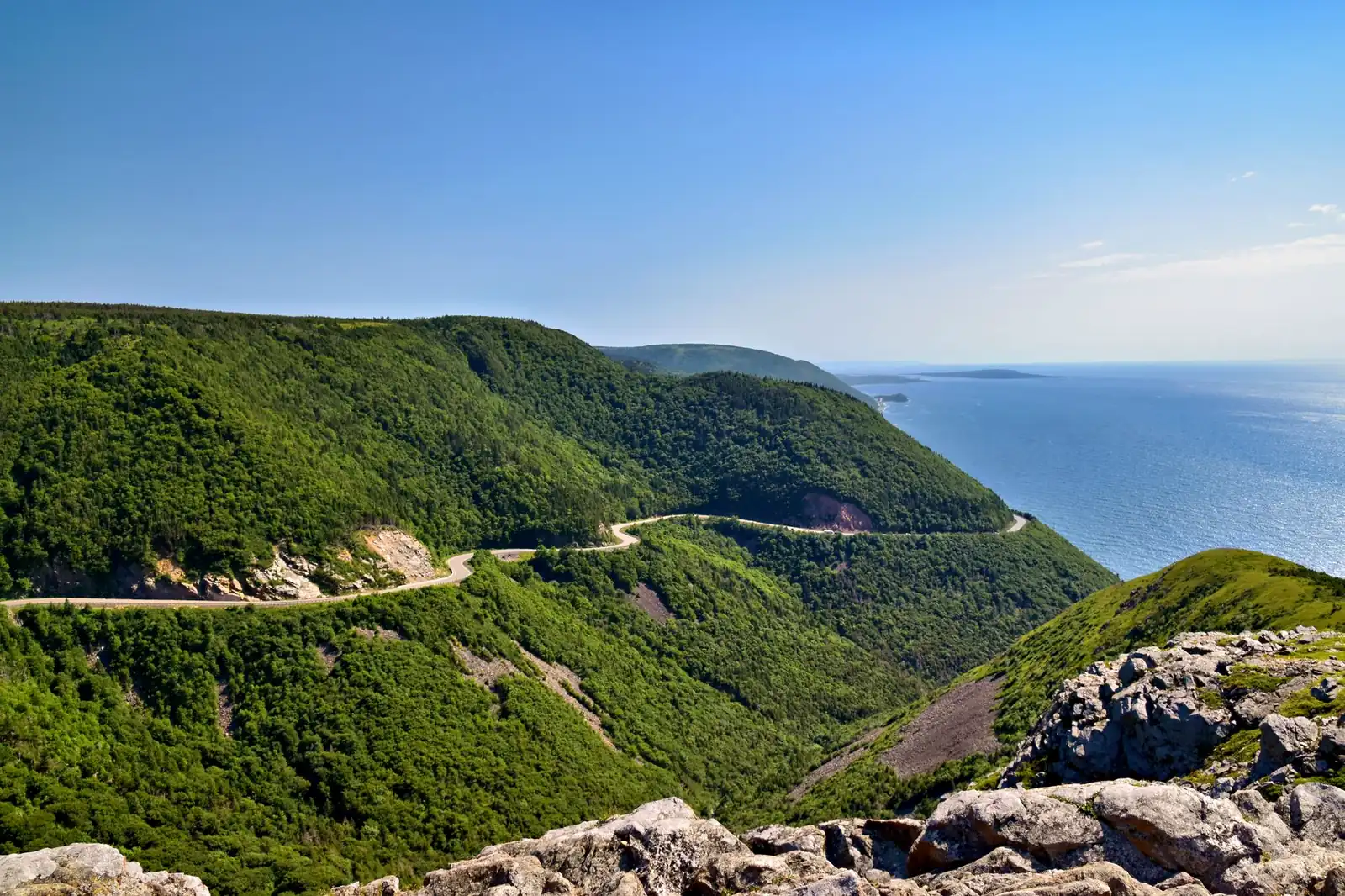 The Cabot Trail winding along Cape Breton's highland coast, green hills dropping to the Gulf of St. Lawrence