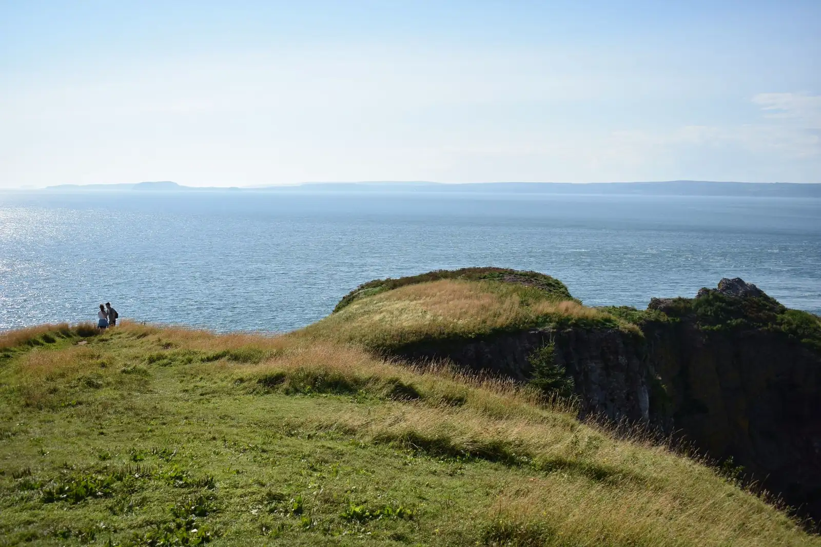 Hikers at a grassy headland cliff overlooking the Gulf of St. Lawrence along the Cape Breton Highlands coast