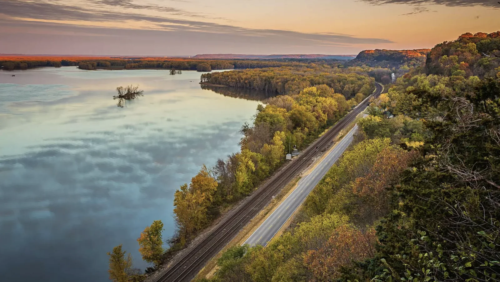 The Great River Road tracing the Mississippi River past autumn-colored bluffs and woodland at sunset