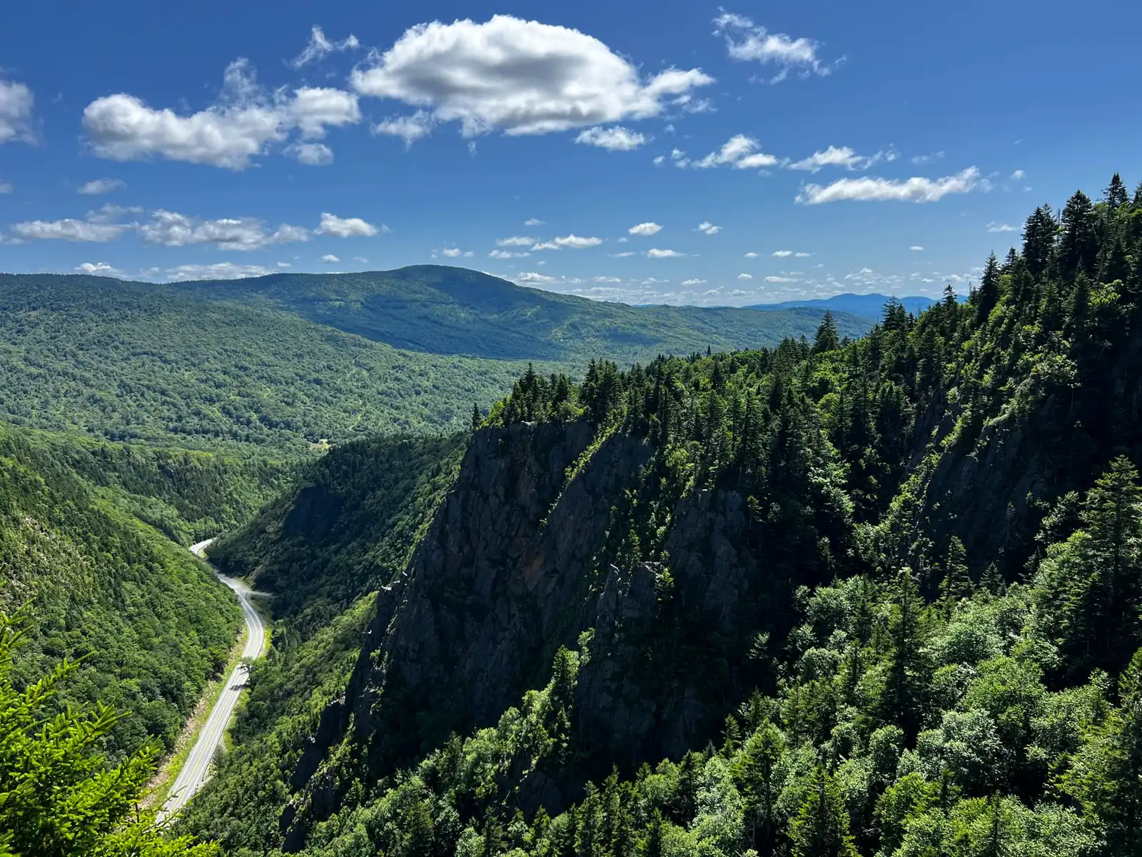 A granite cliff overlook above a two-lane highway winding through a forested White Mountains valley