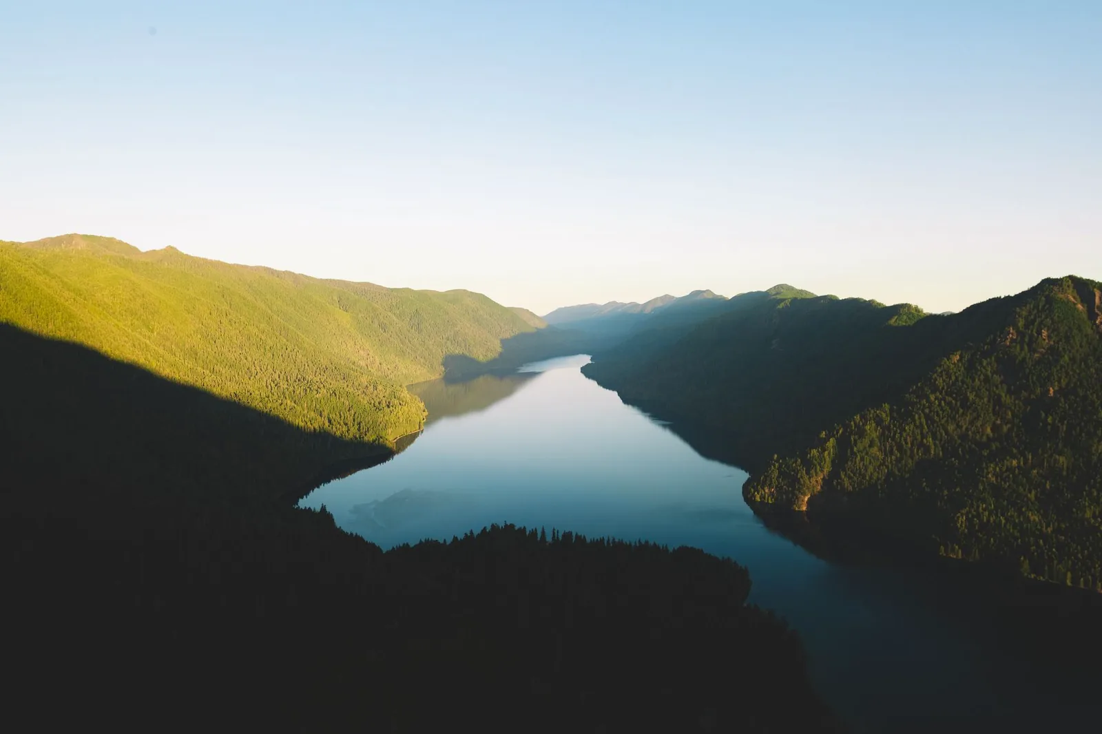 Aerial view at golden hour of a narrow, glacier-carved lake winding between steep forested ridges