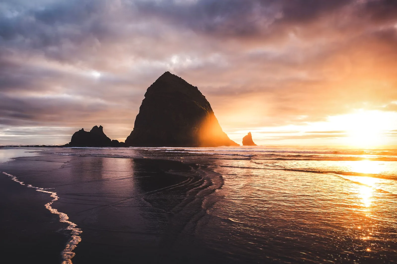 Haystack Rock silhouetted at sunset on Cannon Beach, Oregon, with the sun low over the Pacific
