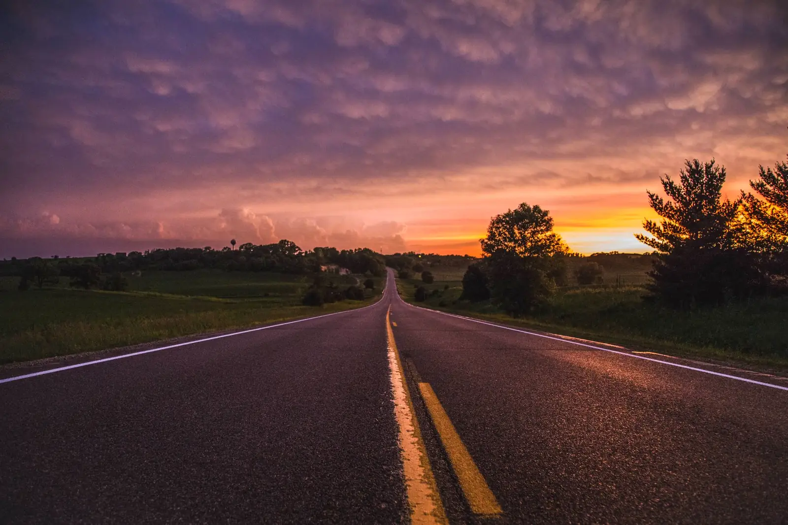 An empty two-lane highway running dead straight to the horizon under a big prairie sky at sunset, the kind of long open stretch a cross-country Trans-Canada crossing repeats for thousands of kilometres