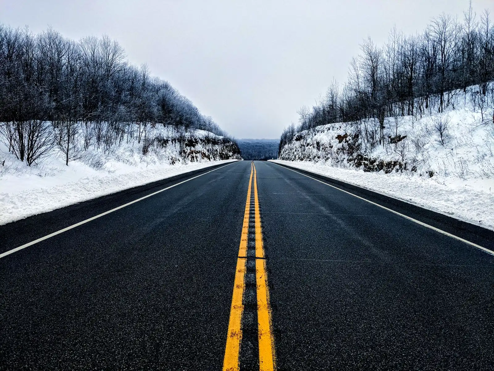An empty two-lane highway cutting straight through a snow-covered forest, symmetrical tree lines on both sides